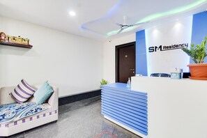 A reception area with a sofa, a reception desk, a ceiling fan, and a door. - Hotel O SM Residency (Bangalore)