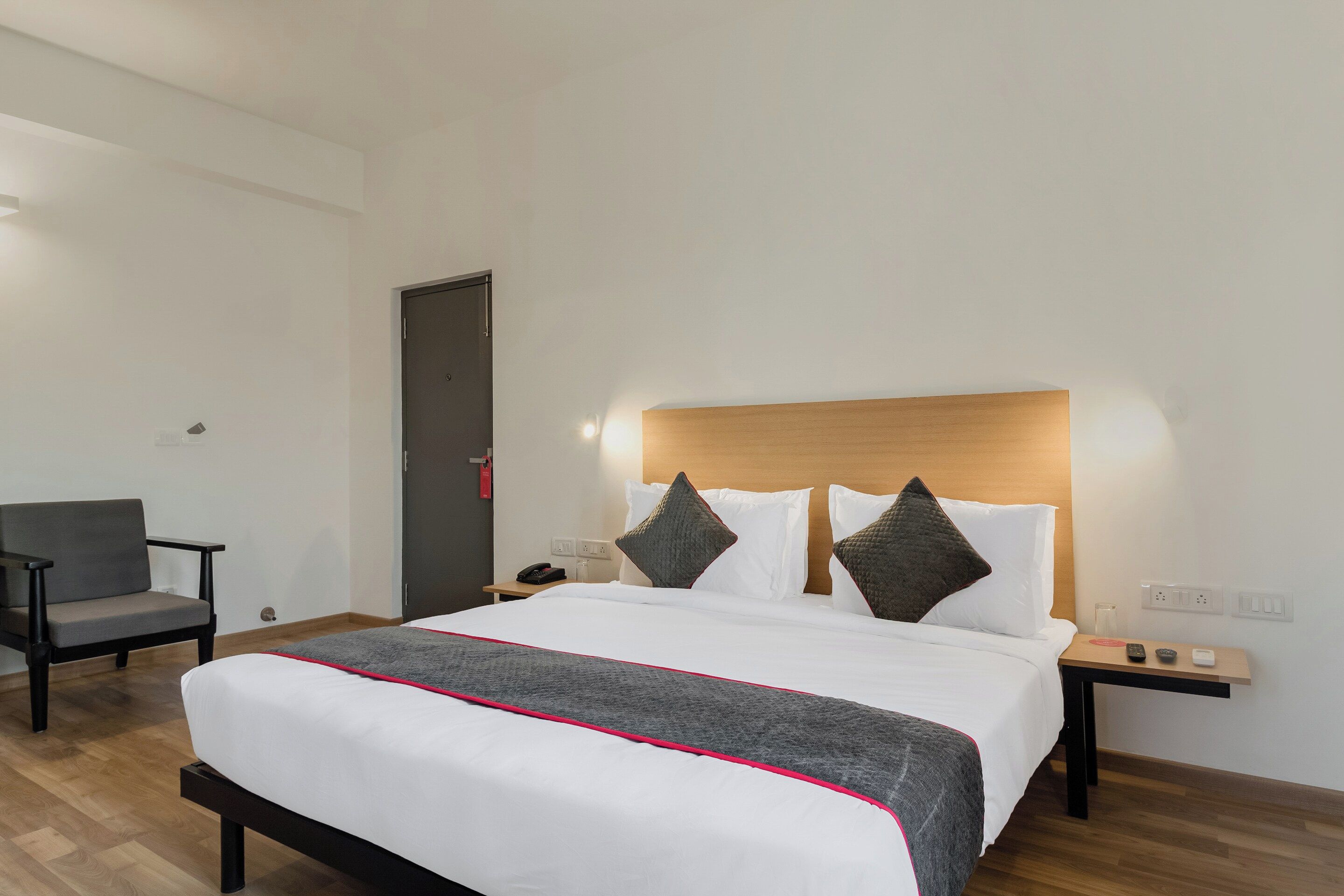 A hotel room with a bed, bedside table, chair, and a door.