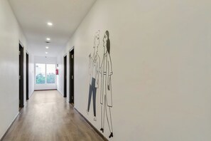 A hallway with a wooden floor, white walls, and a large abstract mural. - Hotel O Rammurthinagar (Bangalore)