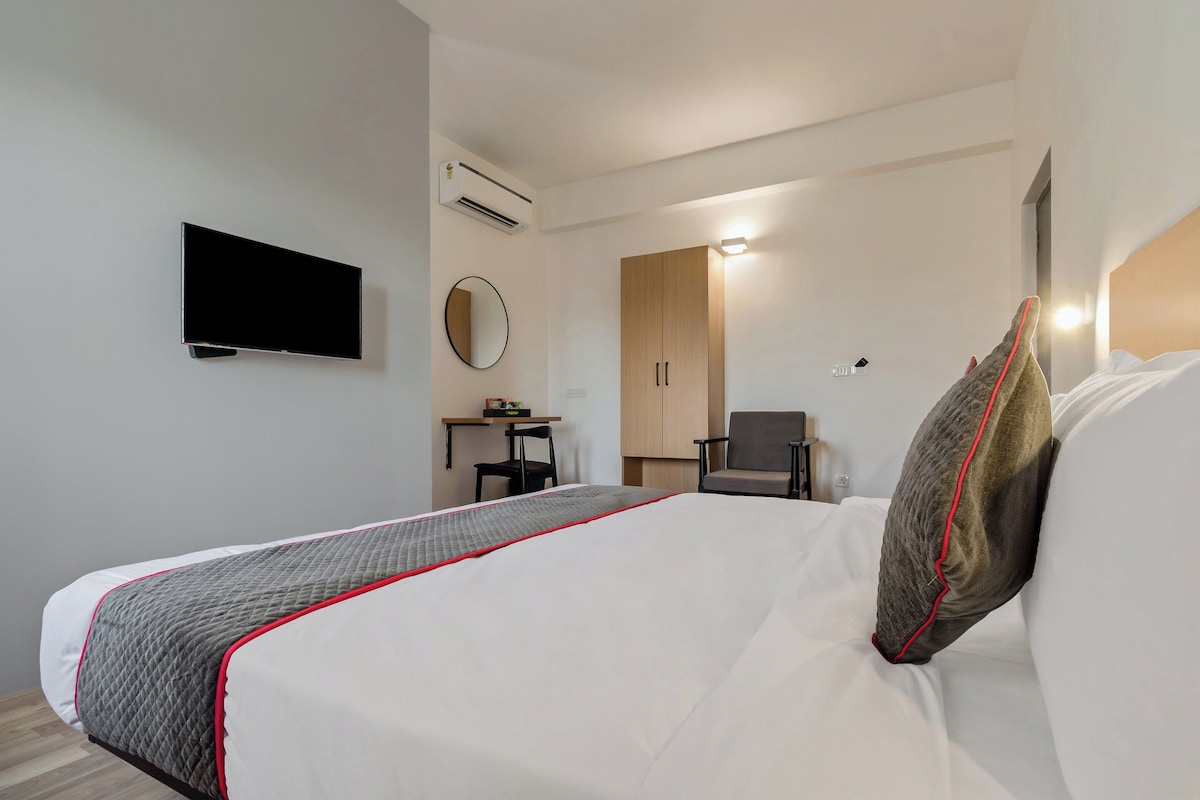 A hotel room with a bed, a TV, a desk, a chair, and a wardrobe.
