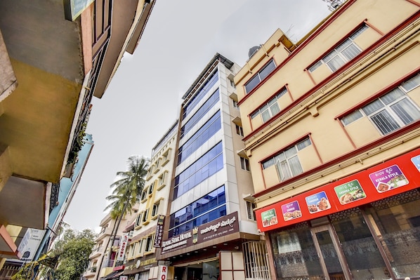 A multi-story hotel with a modern facade, multiple balconies, and a variety of signage indicating different hotel services and local cuisine. - Hotel O Ommiyo Stay. (Bangalore)