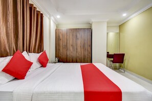 A hotel room with a large bed, a wooden wardrobe, a desk with a chair, and a mirror on the wall. - Hotel O Ommiyo Stay. (Bangalore)
