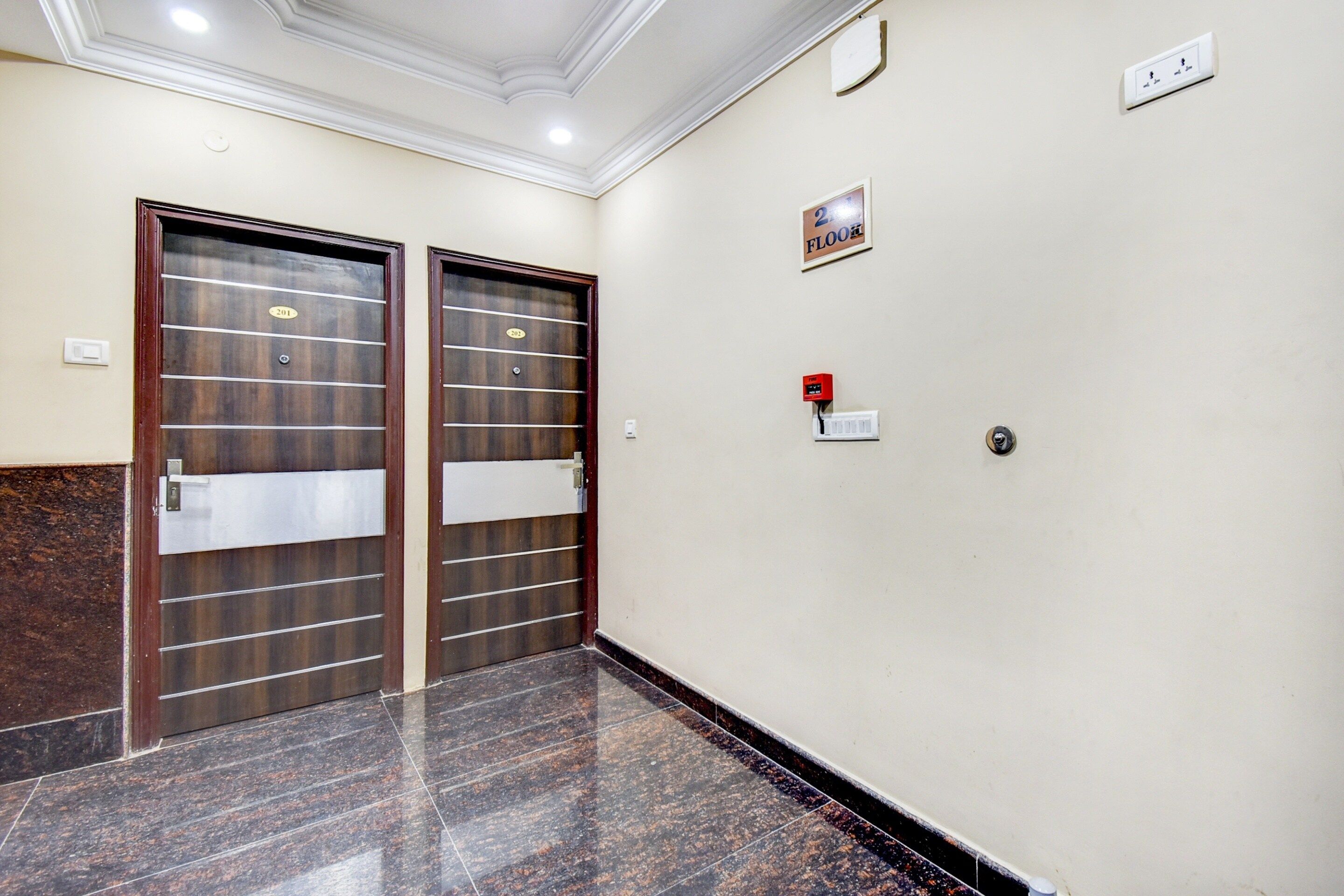 Un pasillo con dos puertas, un detector de incendios y un cartel en la pared.