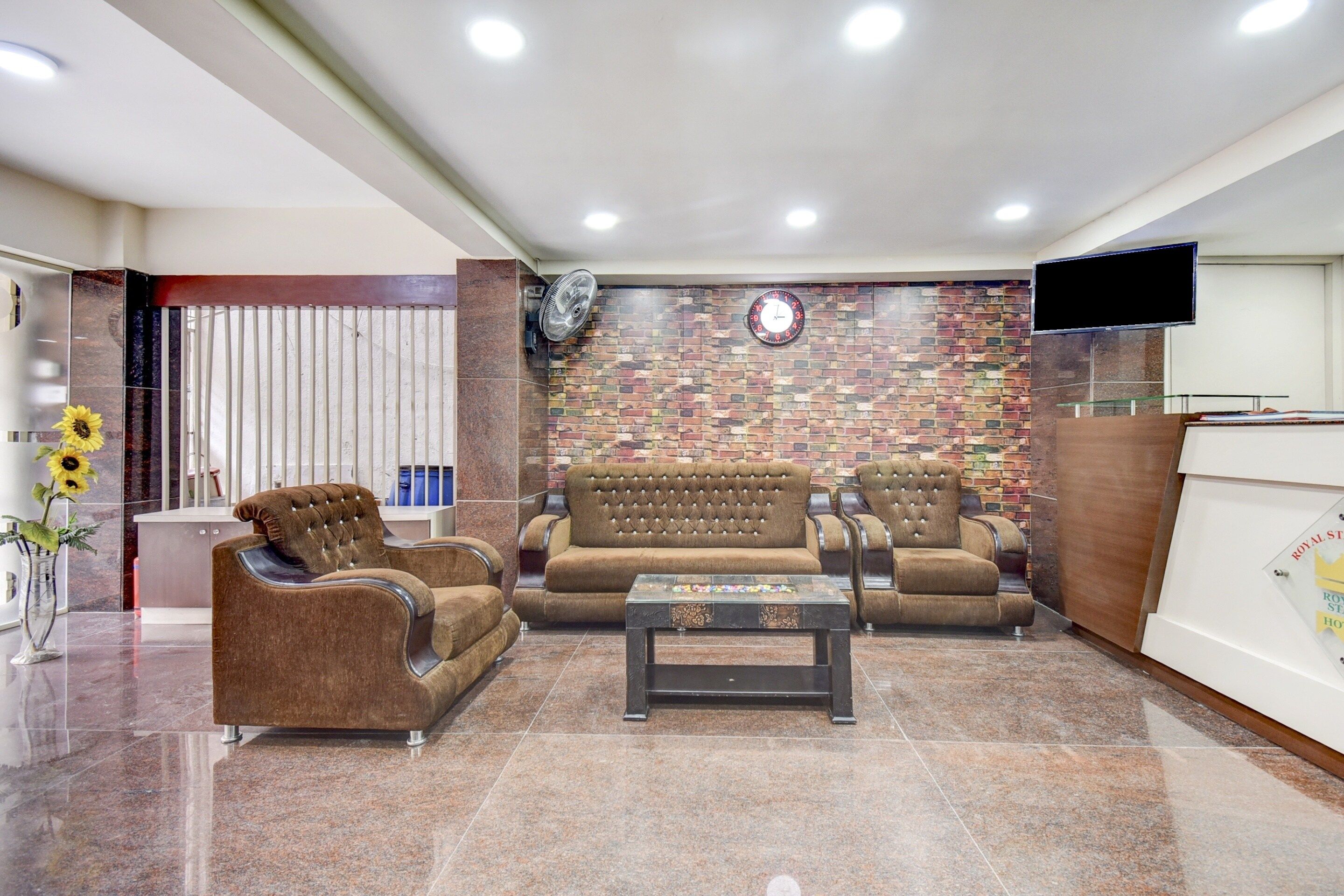 Un hall de hotel con una recepción, un conjunto de sofás, una mesa de centro y un reloj en la pared.