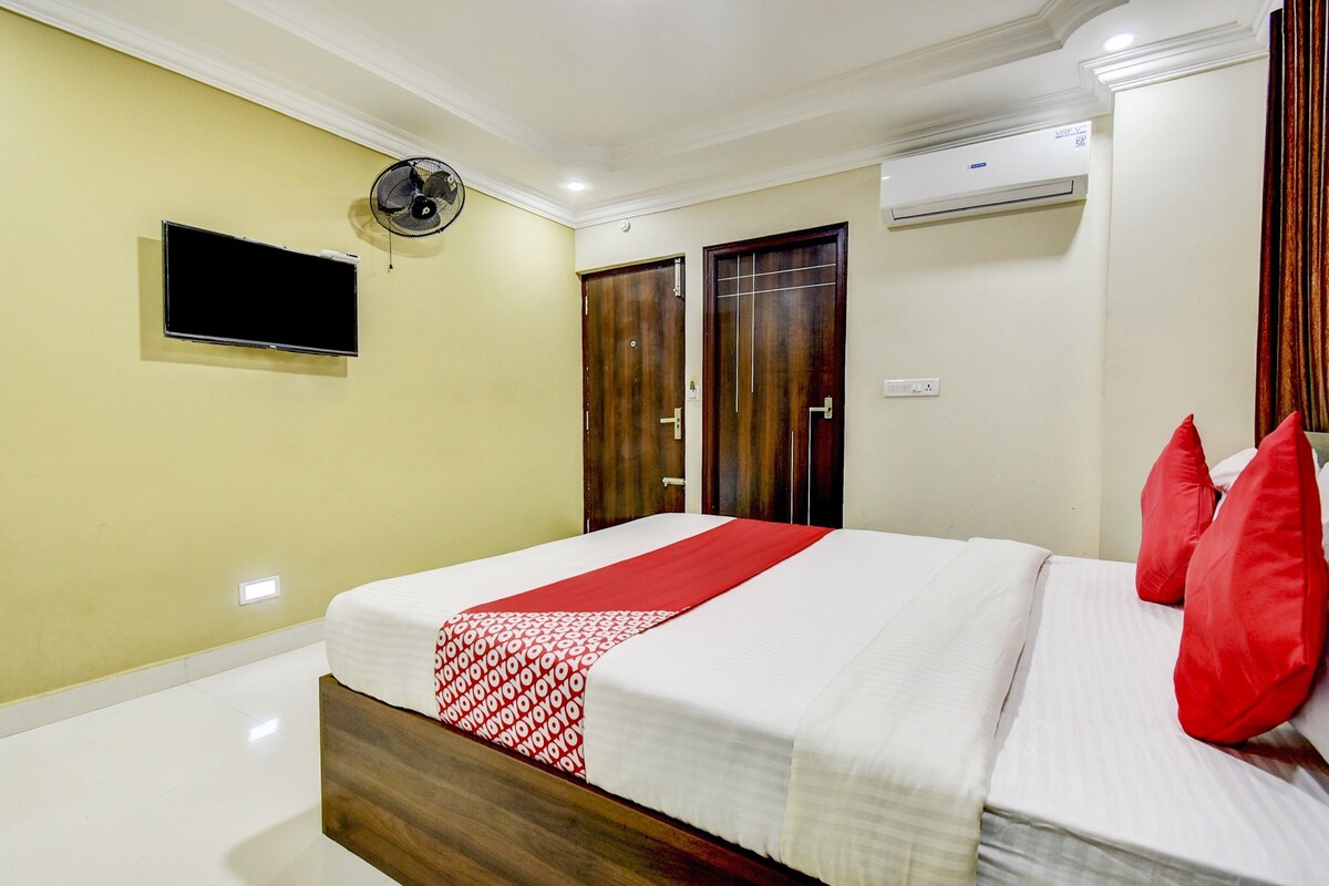Habitación de hotel con cama, televisión, ventilador de techo y aire acondicionado.