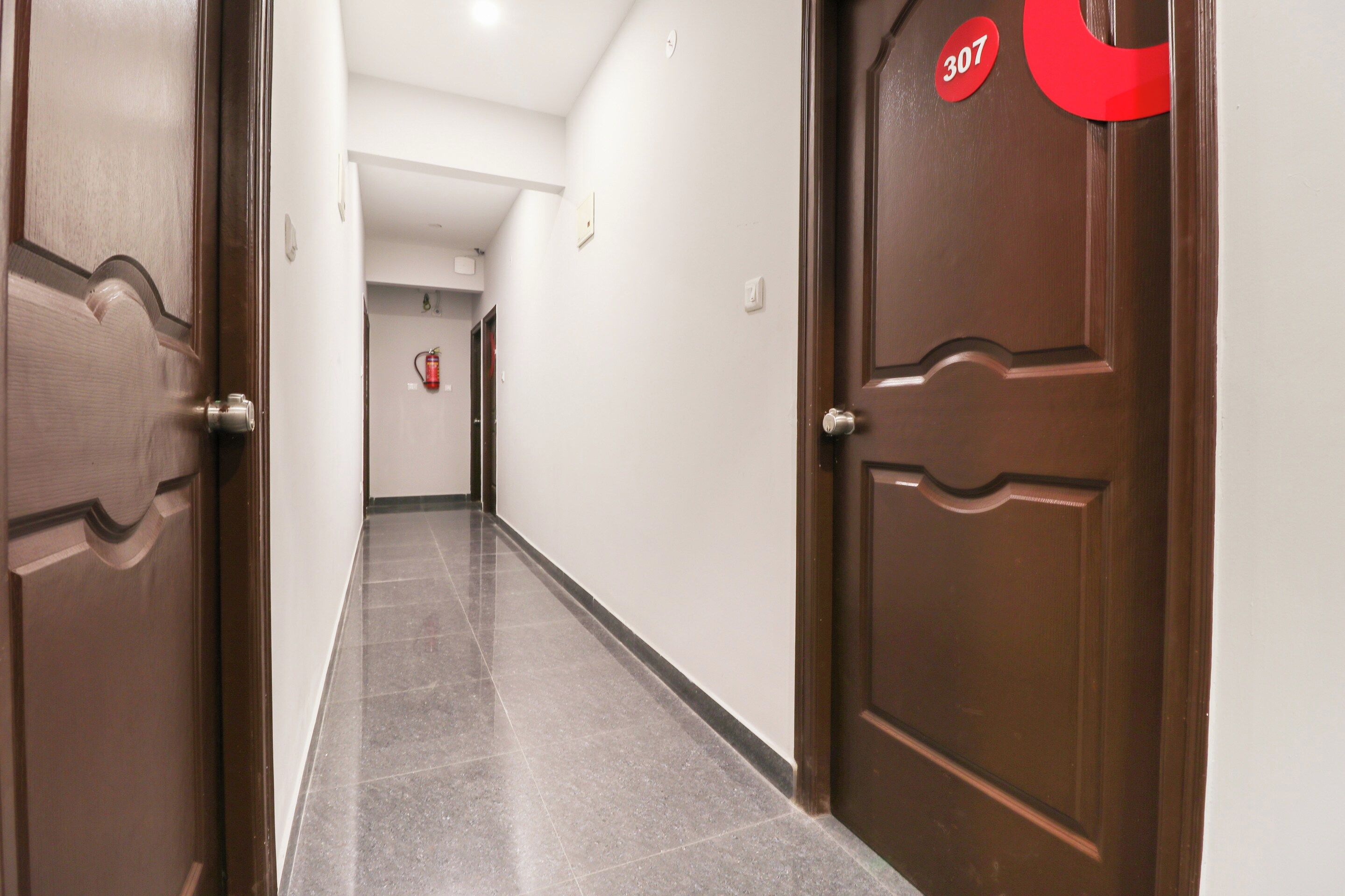 Un pasillo con dos puertas de madera, una con el número 307, que conduce a una habitación con un extintor en la pared.