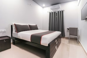 Un dormitorio moderno con una cama, una silla, un equipo de aire acondicionado y un televisor en la pared.