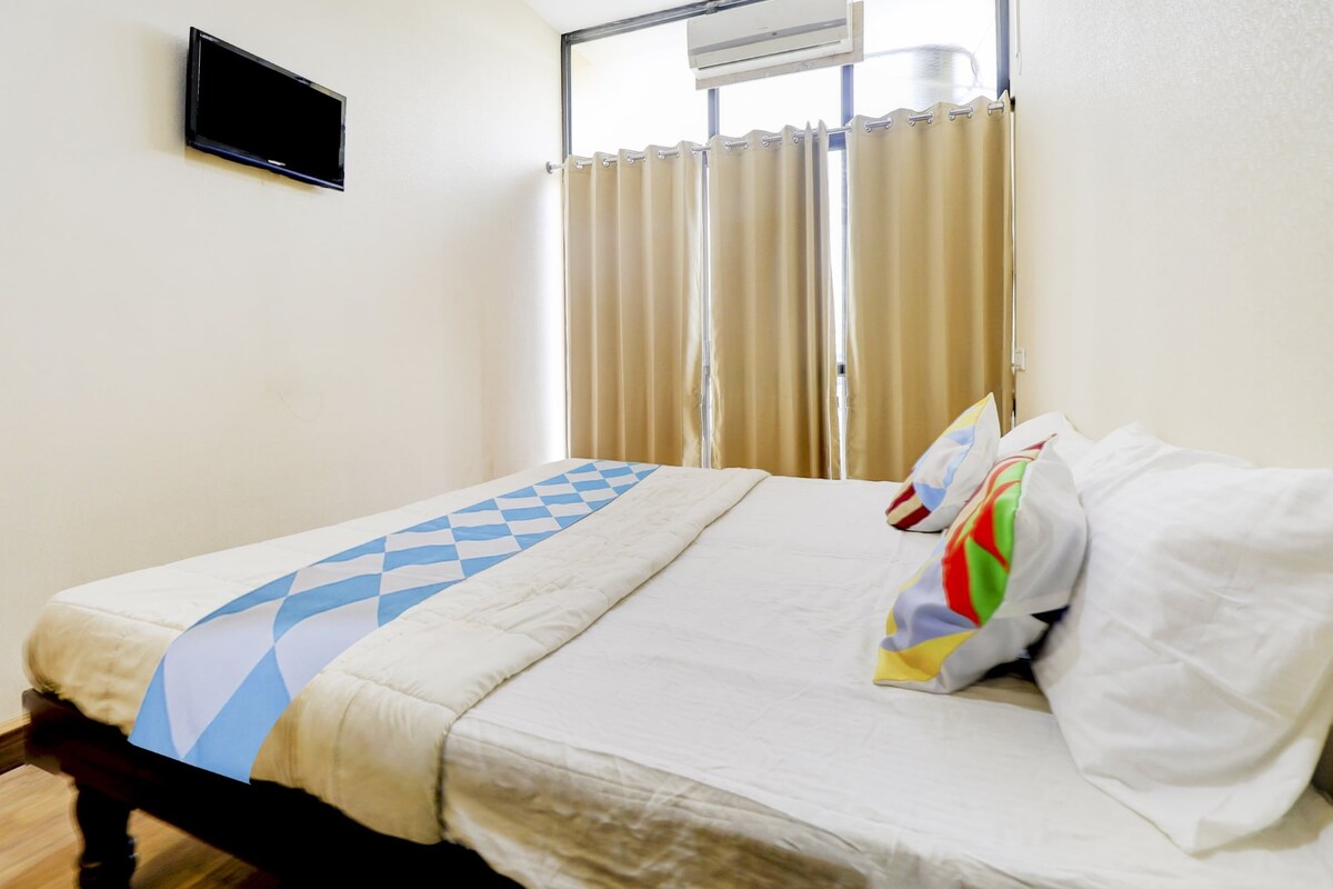 A hotel room with a bed, a flat-screen TV mounted on the wall, and a window with curtains.
