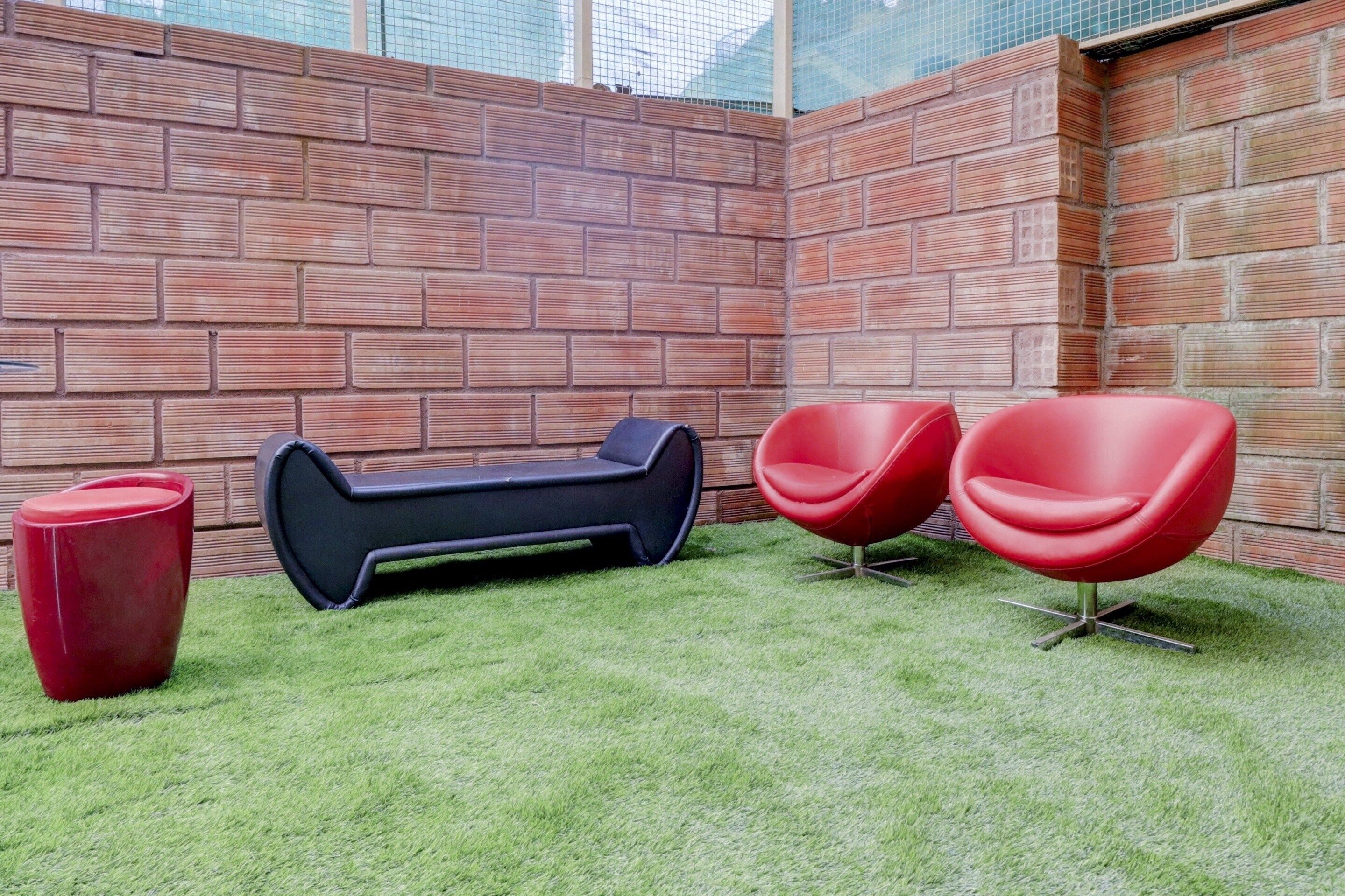 Un área de estar moderna al aire libre con un muro de ladrillo de fondo, un sillón negro y dos sillas rojas.