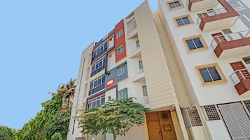 Un edificio residencial de varios pisos con un diseño moderno, que cuenta con balcones, ventanas grandes y un letrero comercial visible en la planta baja.