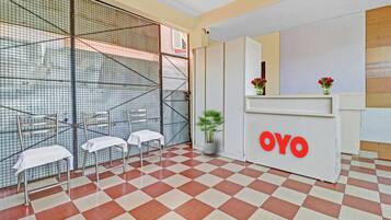 A reception area with a checkered floor, a reception desk with the logo 'OYO', two chairs with white covers, and a potted plant.