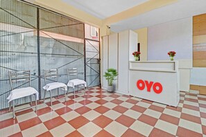 A reception area with a checkered floor, a reception desk with the logo 'OYO', two chairs with white covers, and a potted plant. - Hotel O Mn Residency Near Ragigudda Sri (Bangalore)