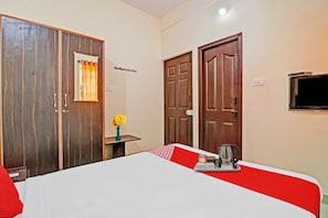 A hotel room with a bed, a small table with a kettle and cups, a vase with flowers, and two doors. - Hotel O Mn Residency Near Ragigudda Sri (Bangalore)