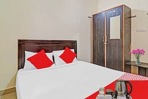 A hotel room with a bed, a wardrobe, a small table with a vase of flowers, and a coffee maker. - Hotel O Mn Residency Near Ragigudda Sri (Bangalore)