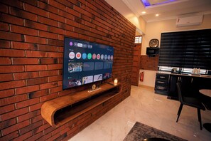 Un soggiorno moderno con una televisione a schermo piatto montata su una parete in mattoni, un mobile porta TV in legno sottostante e un'area pranzo con tavolo e sedie.