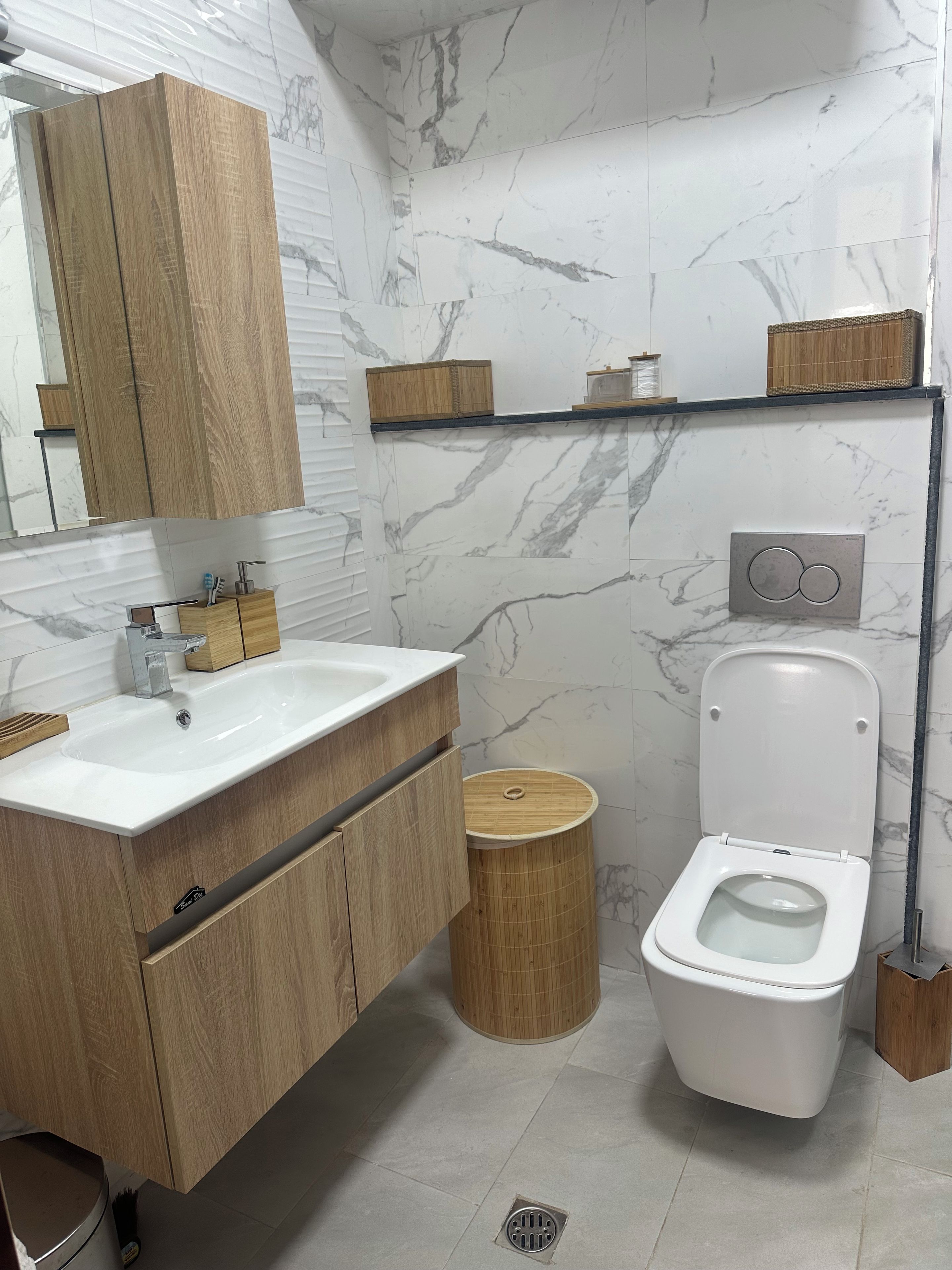 Un bagno moderno con un mobile bagno in legno, un lavandino bianco, un WC e una parete con motivo marmorizzato.