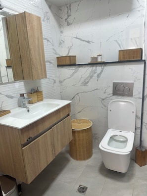 Un bany modern amb un moble de tocador de fusta, un lavabo blanc, un vàter i una paret amb dibuixos de marbre.