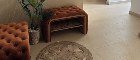 A modern living room with a tufted sofa, a woven rug, and a potted plant.