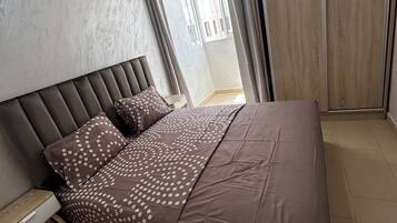 Une chambre à coucher comprenant un lit, une table de chevet, une armoire et une fenêtre avec des rideaux.