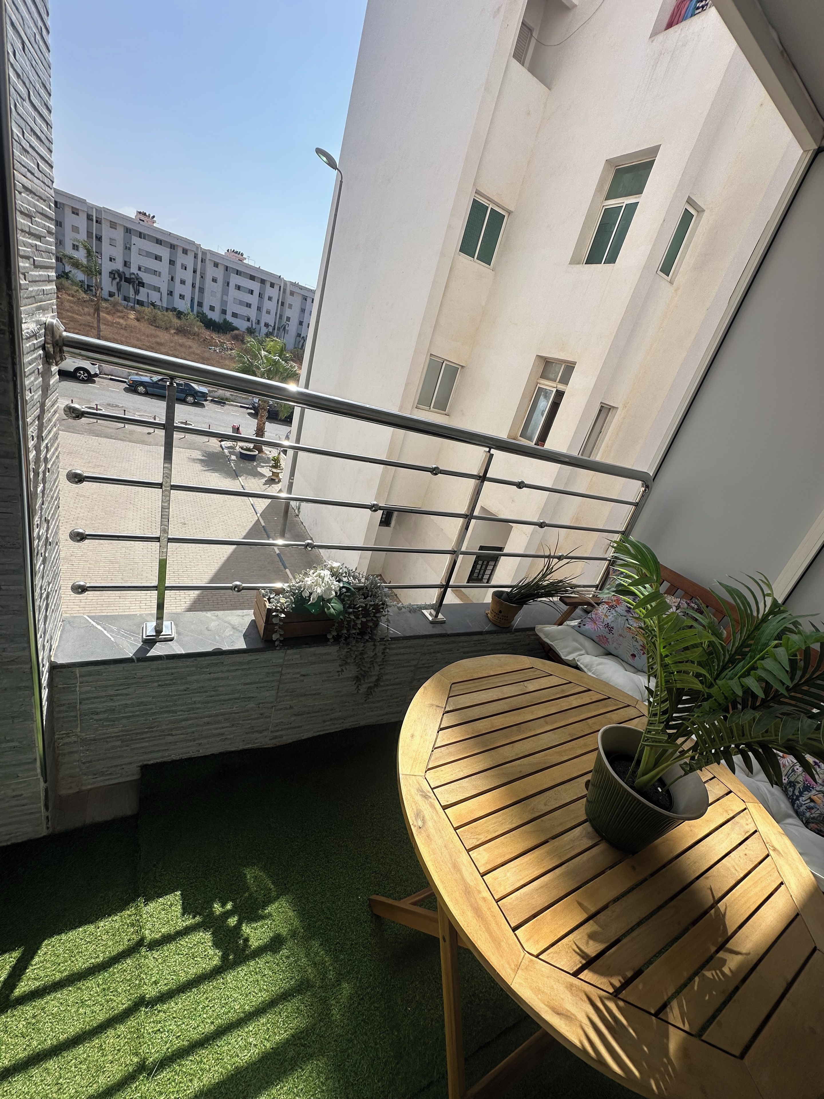 Un balcon avec une balustrade en métal, un pot de fleurs et une table en bois.