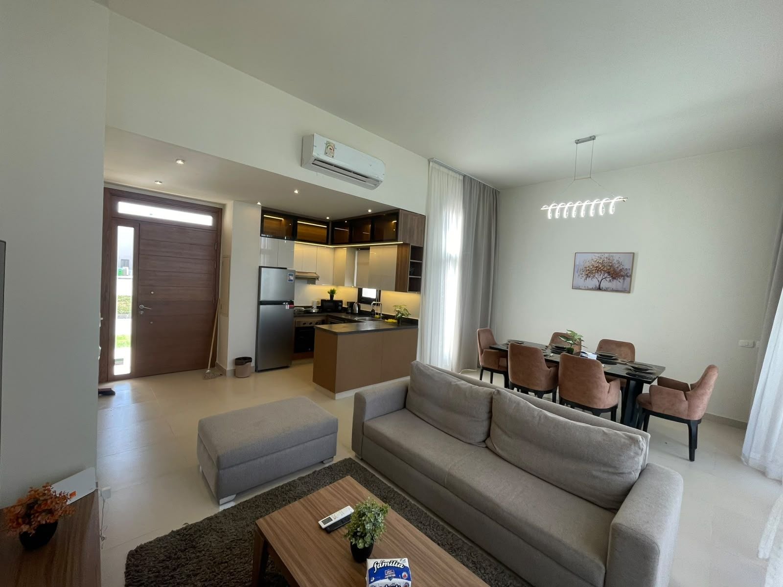 A modern apartment with a living room, kitchenette, dining area, and a large sliding door leading to a balcony.
