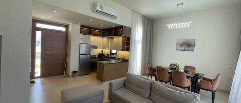 A modern apartment with a living room, kitchenette, dining area, and a large sliding door leading to a balcony.
