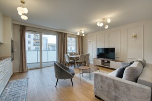 Una sala moderna con sofá, televisión, comedor y ventanas amplias.