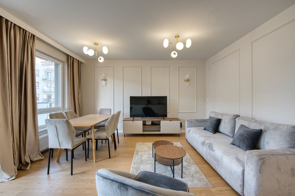 Una sala de estar moderna con mesa de comedor, sofá, televisor e iluminación decorativa.