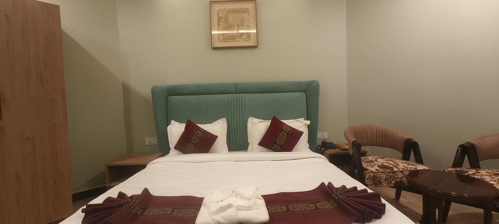 A hotel room with a bed, two chairs, a small table, and a framed picture on the wall.