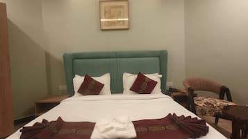 A hotel room with a bed, two chairs, a small table, and a framed picture on the wall.