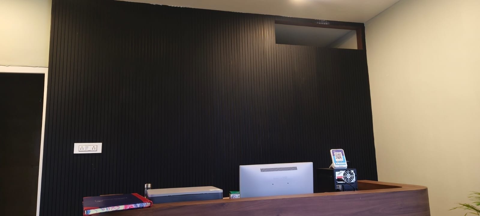A reception desk with a computer, a QR code scanner, and a small plant.