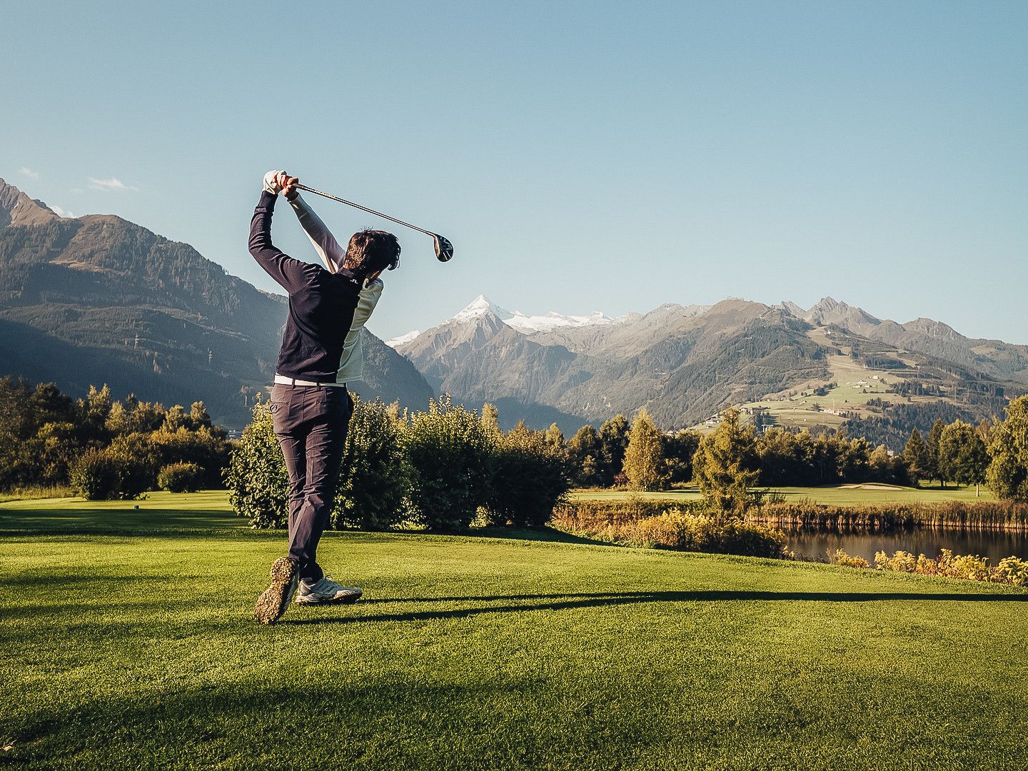 Una persona gioca a golf su un percorso ben curato, con montagne sullo sfondo.