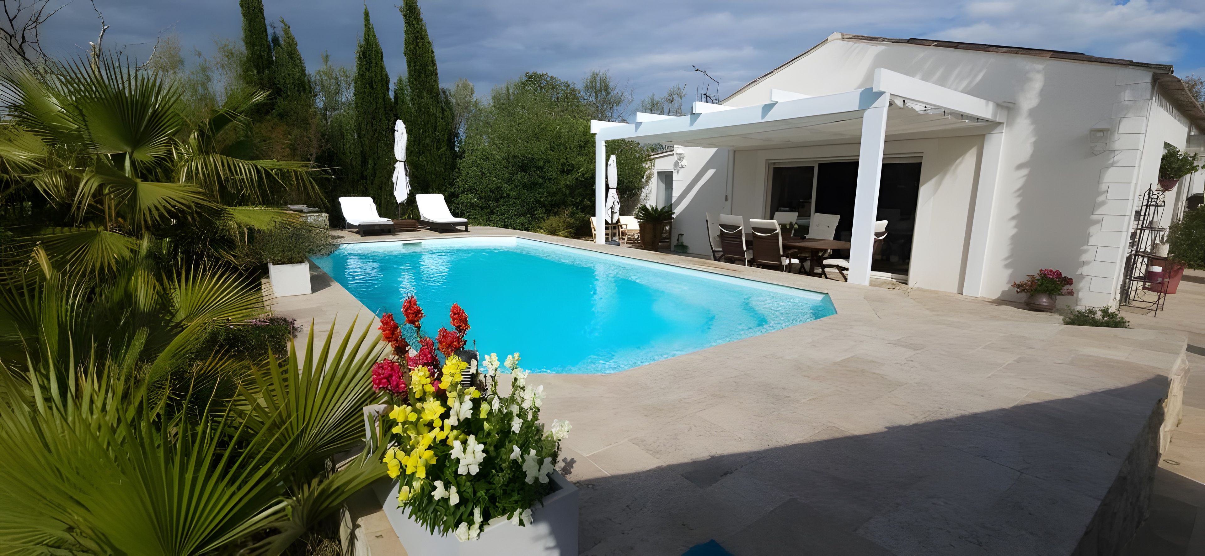 Una piscina con lettini, un portico coperto e un giardino con diverse piante.