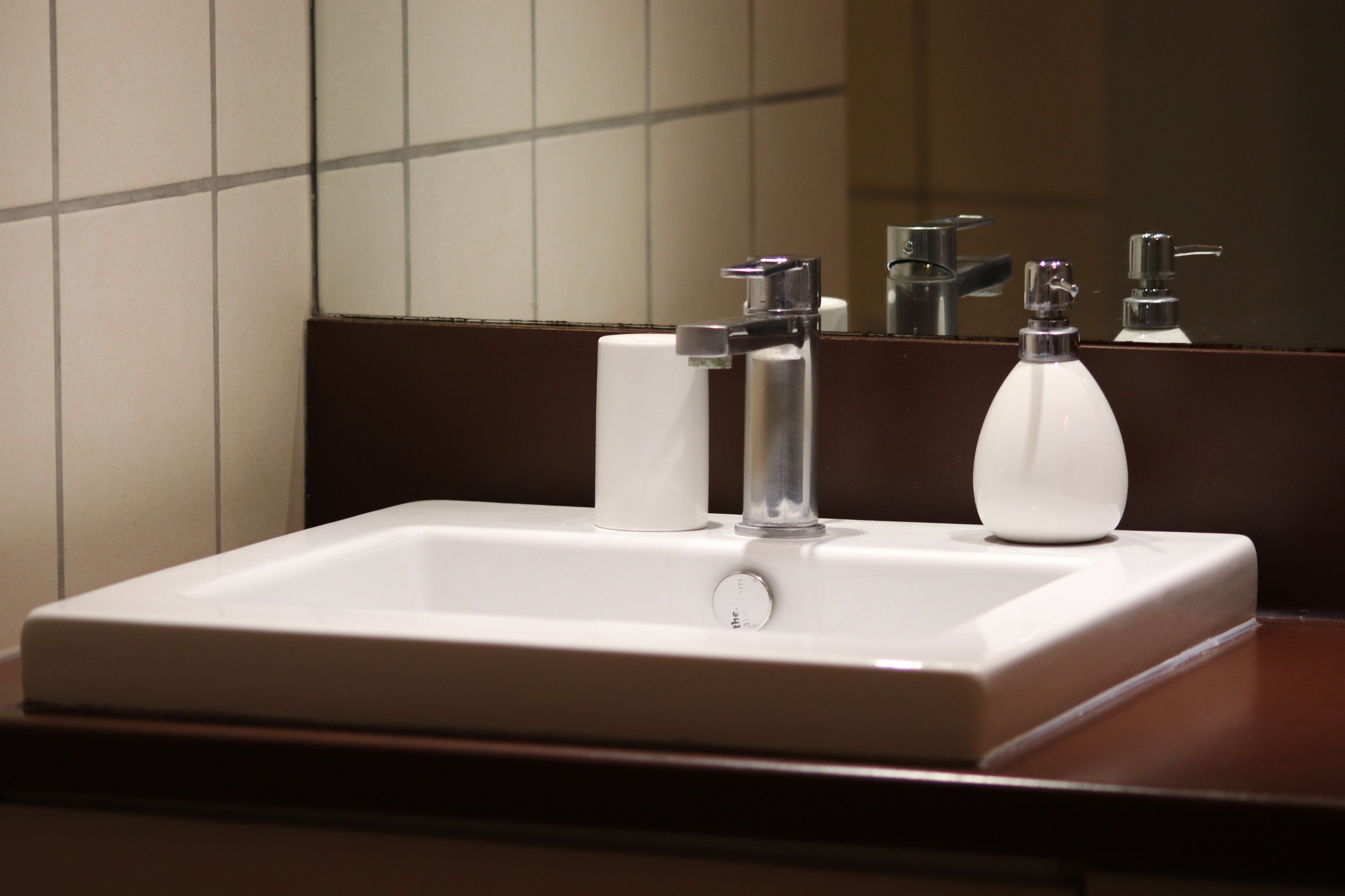 Un bagno con un lavandino bianco, due rubinetti e uno specchio.