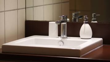 Un bagno con un lavandino bianco, due rubinetti e uno specchio.