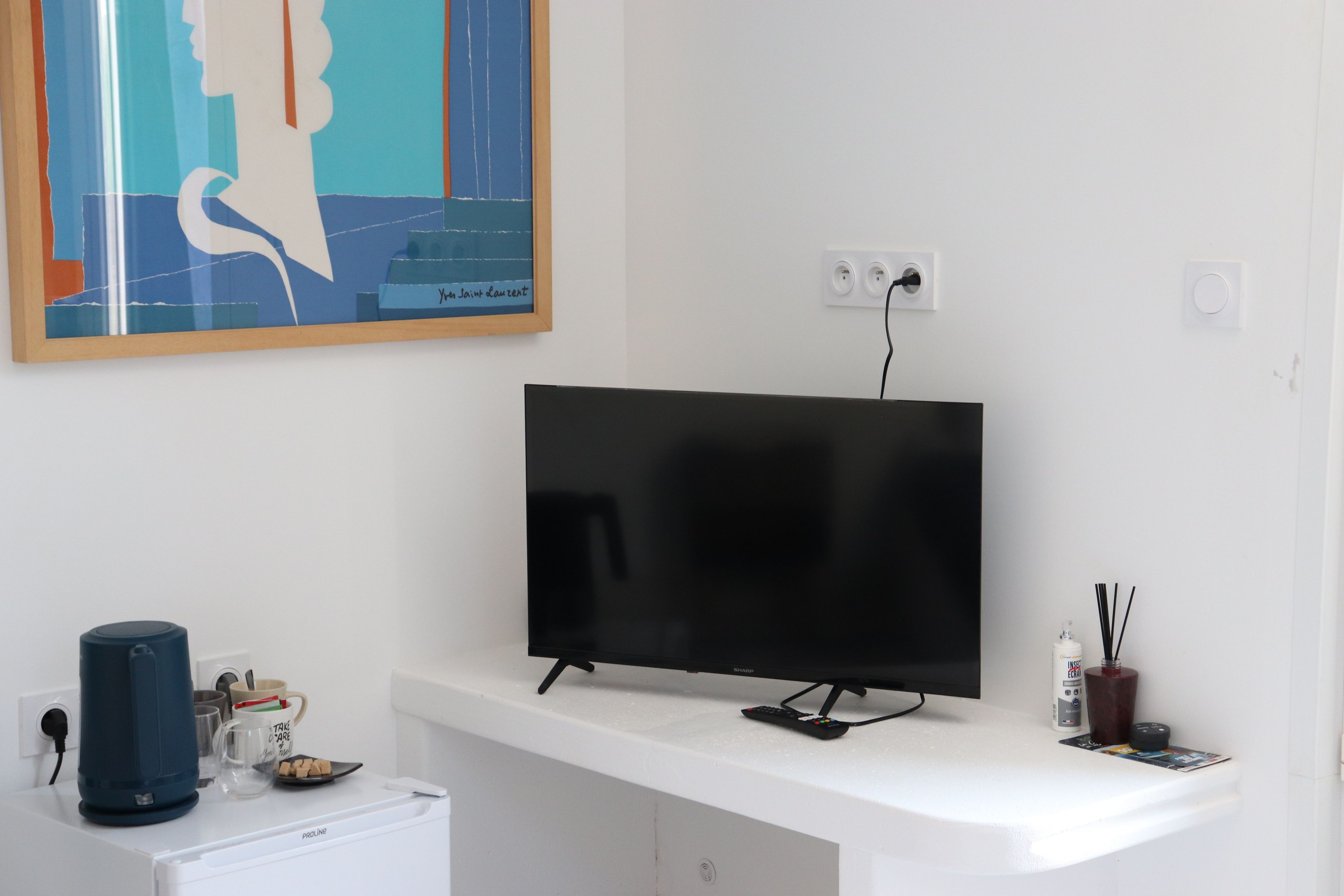 Un soggiorno moderno con una TV a schermo piatto su un supporto bianco, una macchina per caffè, una tazza e un telecomando.