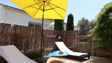 Un patio con due poltrone, un ombrellone giallo e un tavolino.