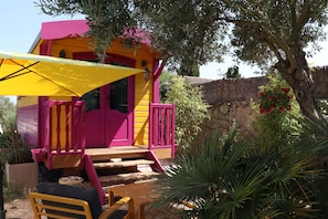 A colorful outdoor seating area with a wooden bench and a yellow umbrella. - Gitane Caravan, Tiny House with Private Terrace (Aigues-Mortes)