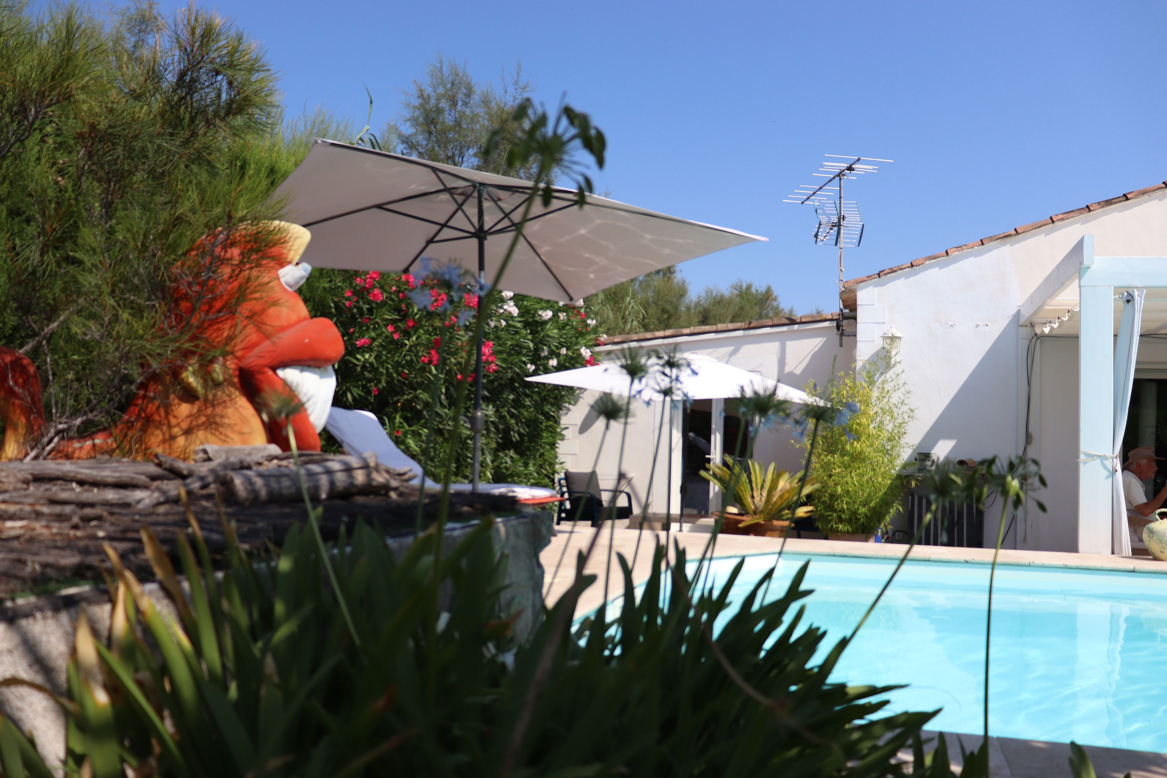 Un espace piscine comprenant une chaise longue, un parasol et une personne assise au bord de la piscine.