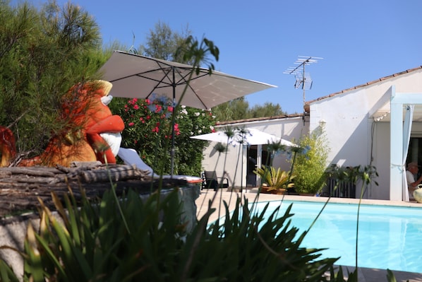 A pool area with a lounge chair, umbrella, and a person sitting by the pool. - Gitane Caravan, Tiny House with Private Terrace (Aigues-Mortes)