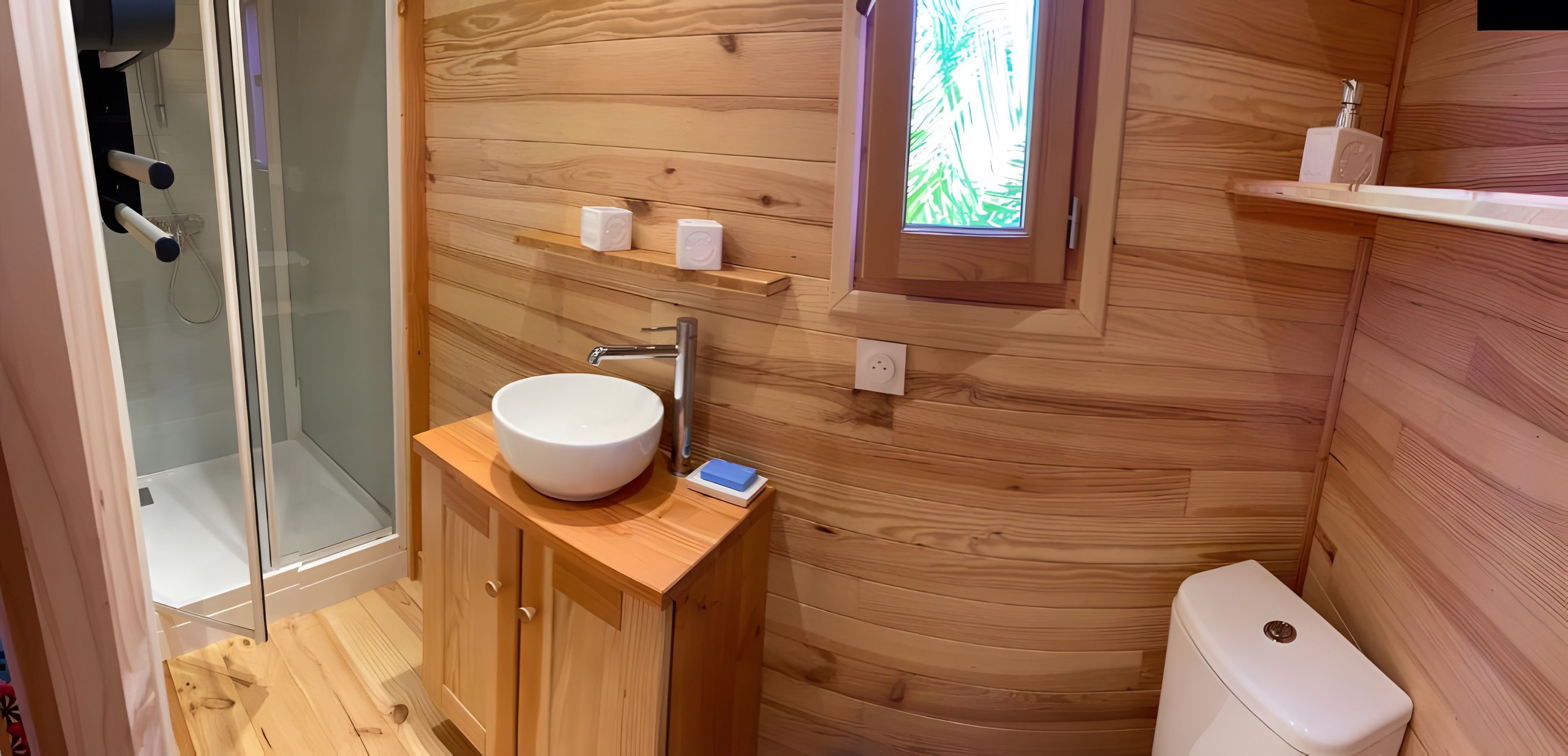 Un bagno con rivestimenti in legno, un lavandino bianco, uno sportello doccia in vetro e un water.