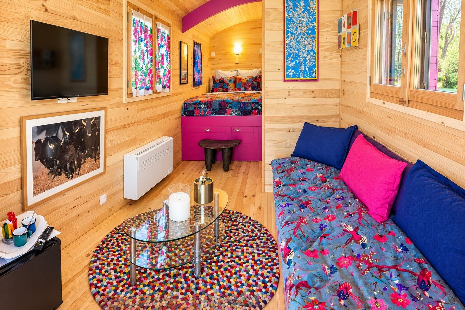 A cozy room with a bed, a sofa, a TV, and a colorful rug.