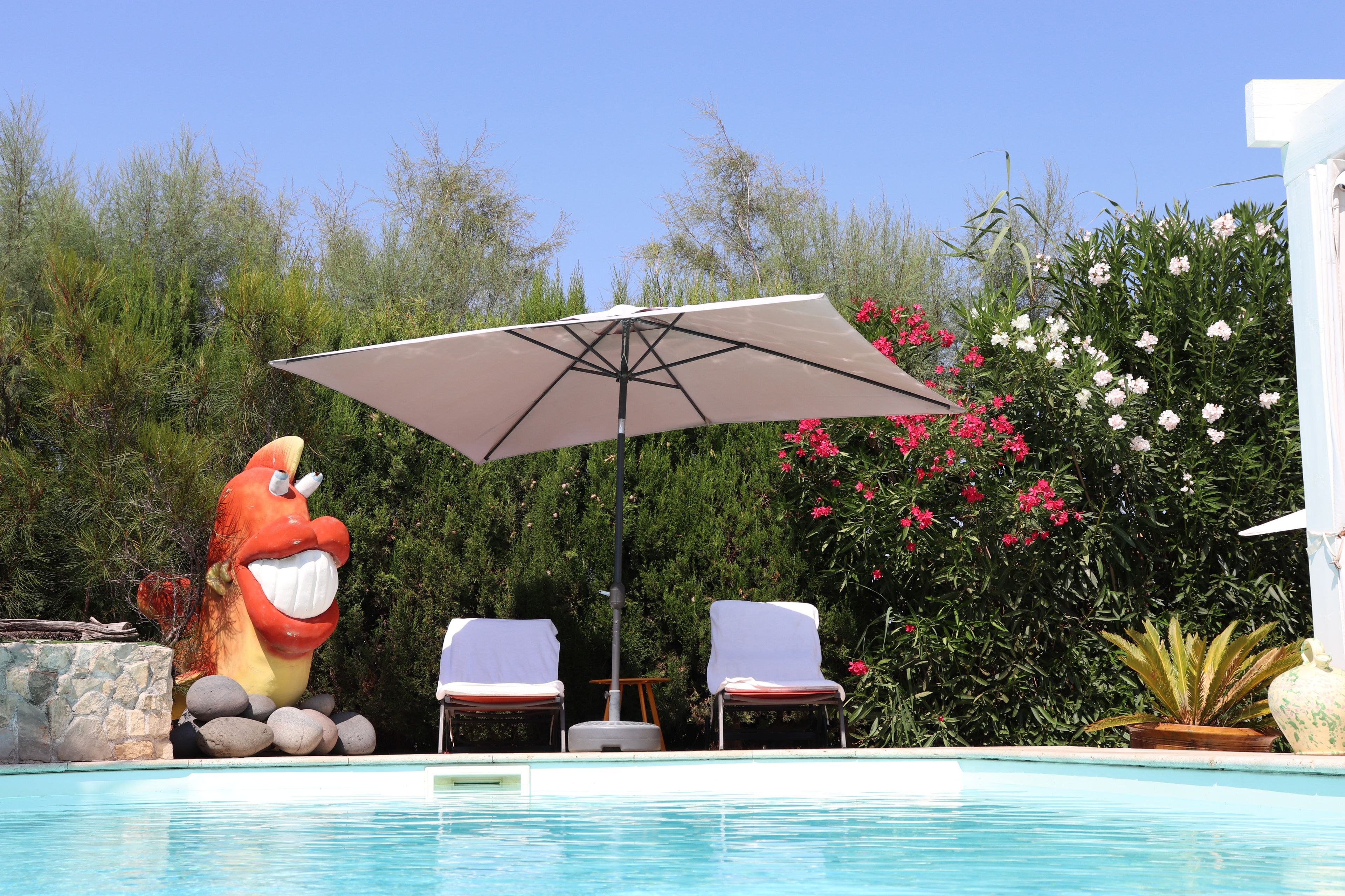 Una piscina con due sdraio e un ombrellone, circondata da vegetazione e una grande statua a forma di personaggio dei cartoni animati.