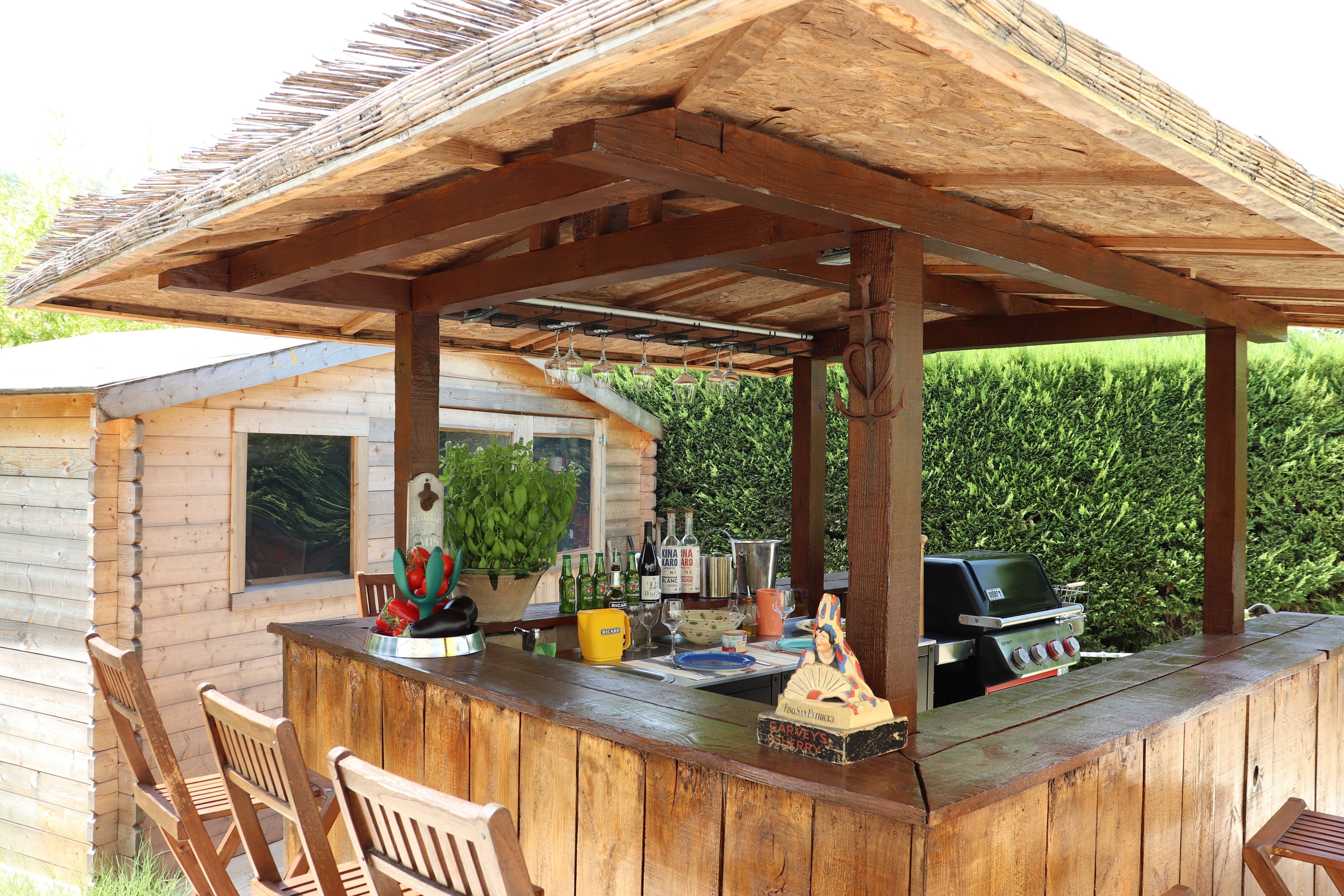 Un'area bar esterna in legno con un pergolato, posti a sedere e un barbecue.