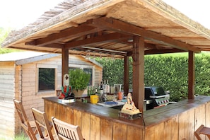 Un'area bar esterna in legno con un pergolato, posti a sedere e un barbecue.