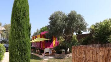 Un cortile recintato con un alto albero sempreverde, un edificio colorato con un ombrello giallo e un muro in pietra.