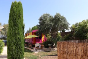 Un cortile recintato con un alto albero sempreverde, un edificio colorato con un ombrello giallo e un muro in pietra.