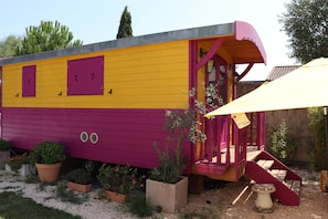 A colorful, single-story building with a yellow and purple exterior, a red door, and a small porch area. - Gitane Caravan, Tiny House with Private Terrace (Aigues-Mortes)