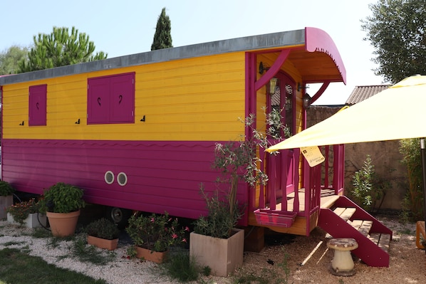 A colorful, single-story building with a yellow and purple exterior, a red door, and a small porch area. - Gitane Caravan, Tiny House with Private Terrace (Aigues-Mortes)