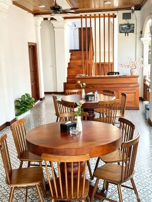 Un coin repas avec une table et des chaises en bois, un vase rempli de fleurs et un escalier en arrière-plan.